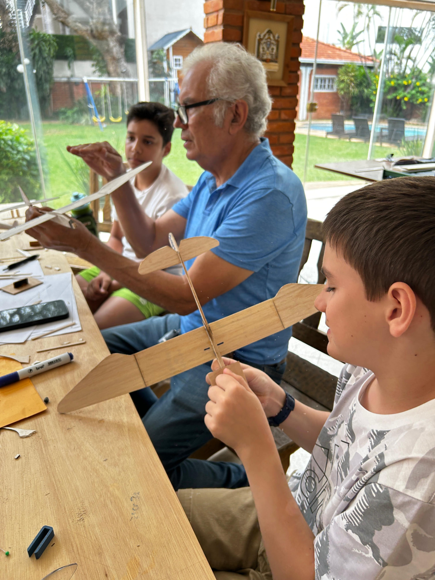 Instructor y dos chicos armando planeadores de madera balsa sobre una mesa de trabajo