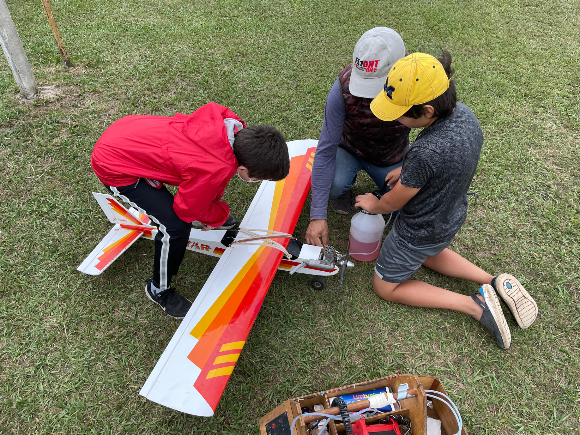 Dos chicos y su instructor preparando el motor a combustión de un aeromodelo en el campo de vuelo