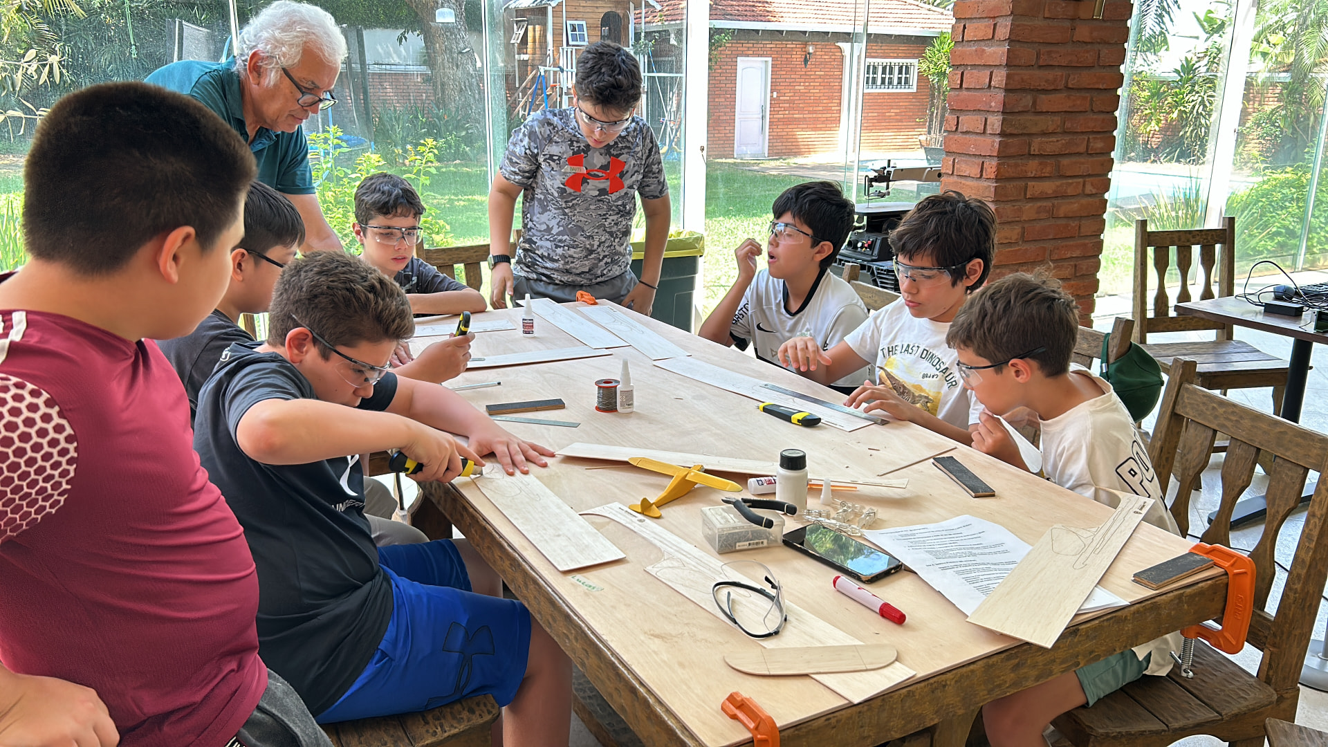 Chicos con lentes de seguridad construyen aviones de aeromodelismo en madera de balsa junto a su instructor